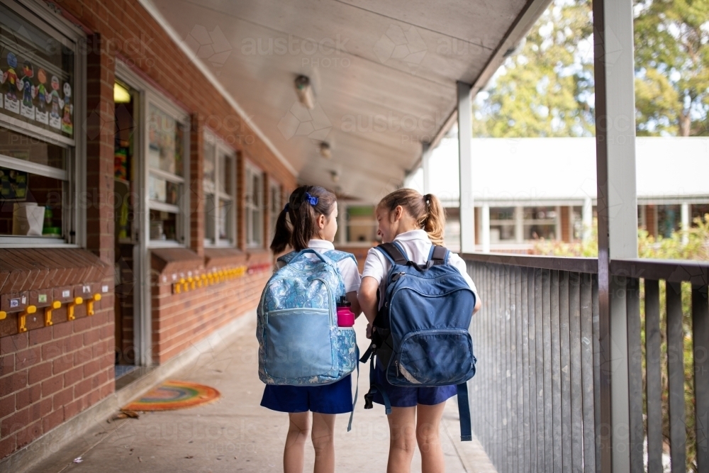 Two young schoolgirls walking along outdoor hallway at school - Australian Stock Image