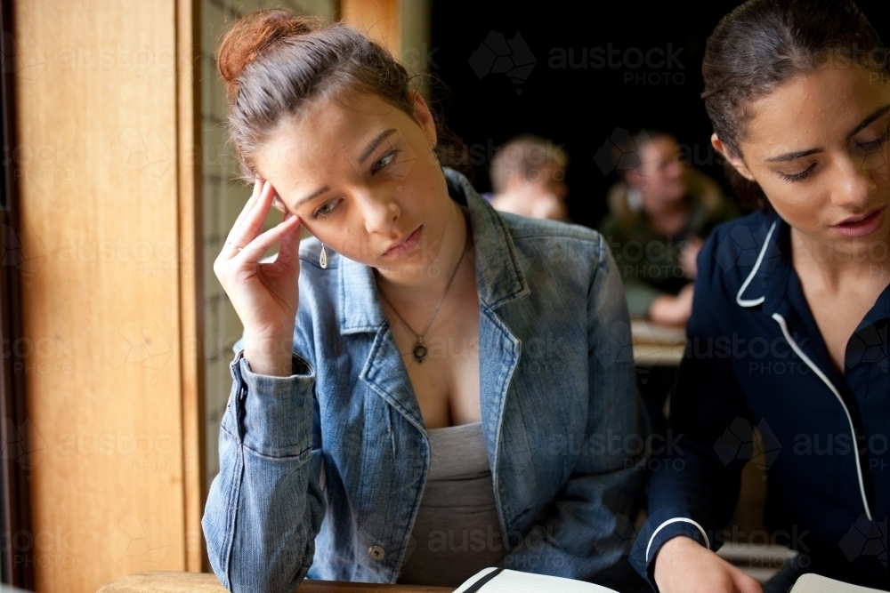 Two young women sitting at a desk in a classroom - Australian Stock Image