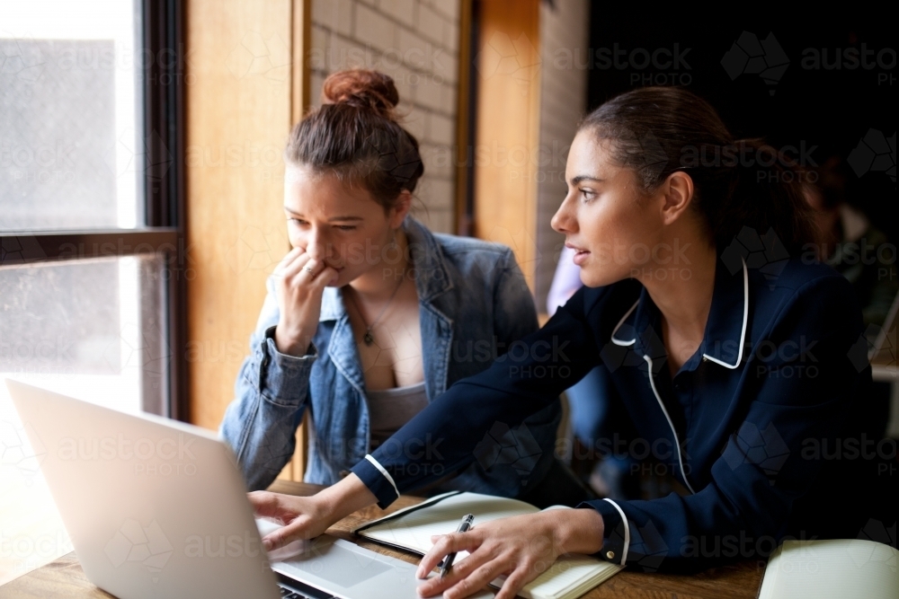 Two young women sitting at a desk in a classroom - Australian Stock Image
