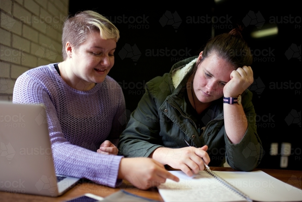 Two young women sitting at a desk in a classroom - Australian Stock Image