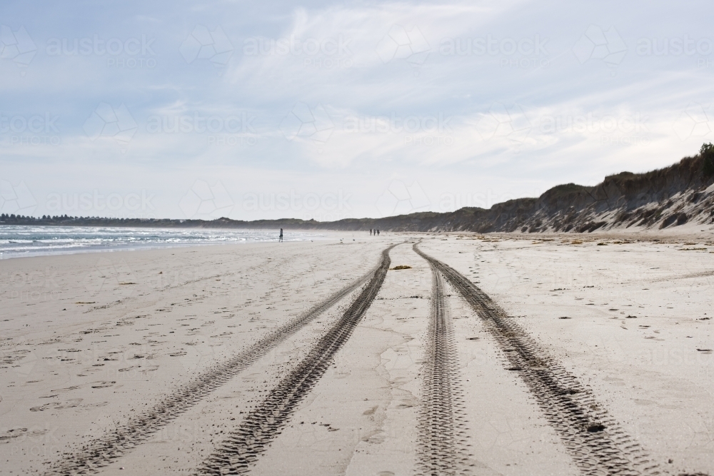 tyre tracks and footprints on a beach with people in distance - Australian Stock Image