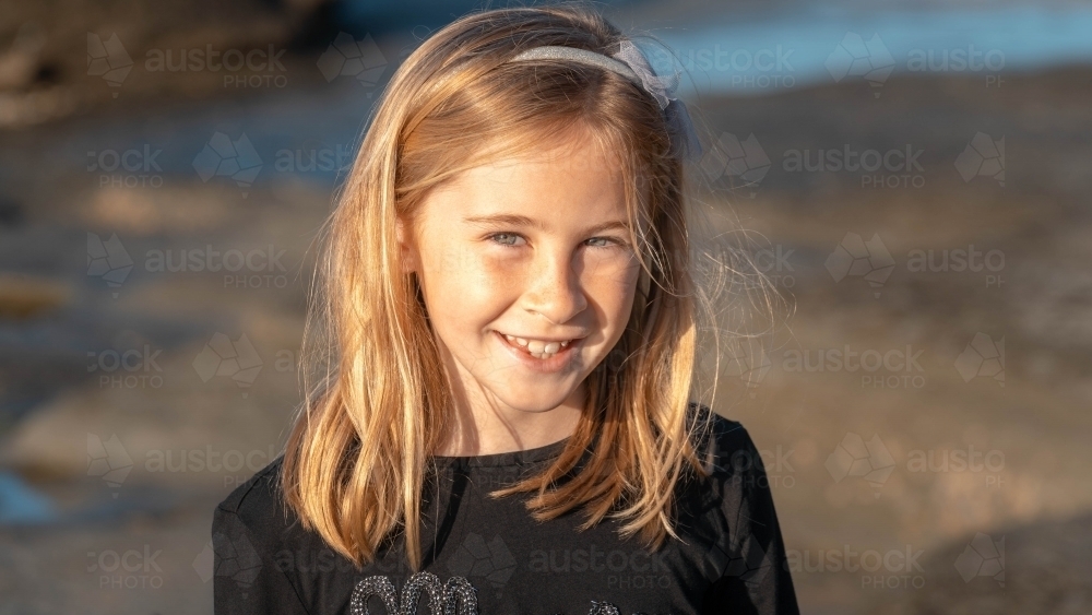 Under 10 girl smiling at camera at sunrise on beach - Australian Stock Image