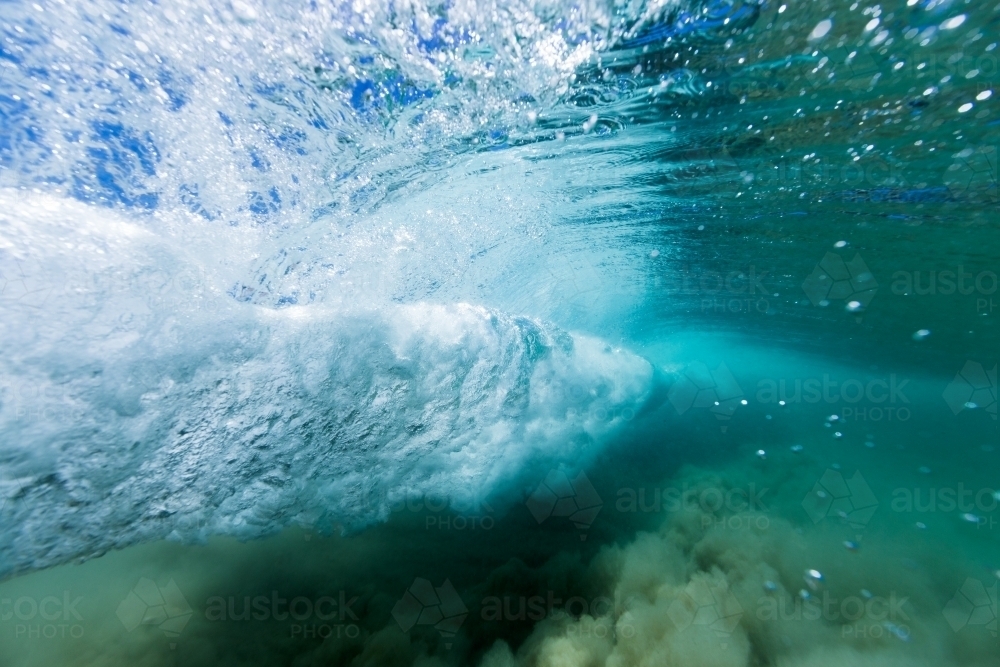 Under water view of an ocean wave breaking in a vortex on sand in crystal clear, blue water. - Australian Stock Image