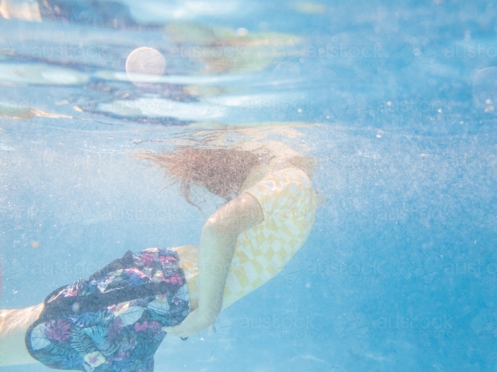Underwater image of girl coming up to breath air in backyard pool while palying - Australian Stock Image