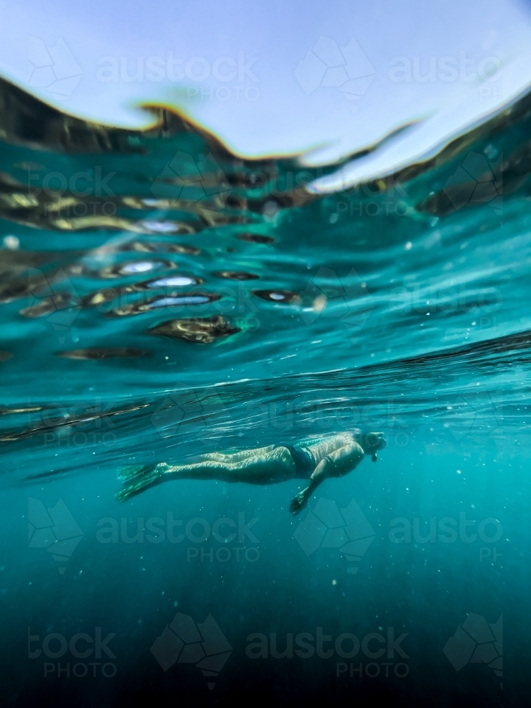 Underwater of female snorkelling in ocean afloat at surface looking down - Australian Stock Image