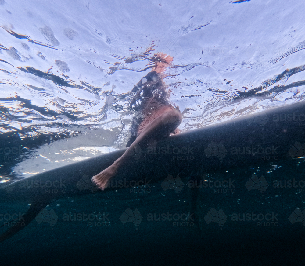 Underwater of females legs sitting on longboard single fin surfboard with good visibility - Australian Stock Image