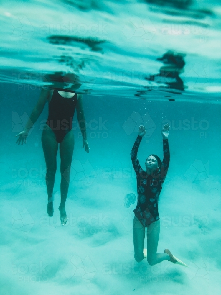 Underwater of two females, one diving under the surface in the ocean - Australian Stock Image