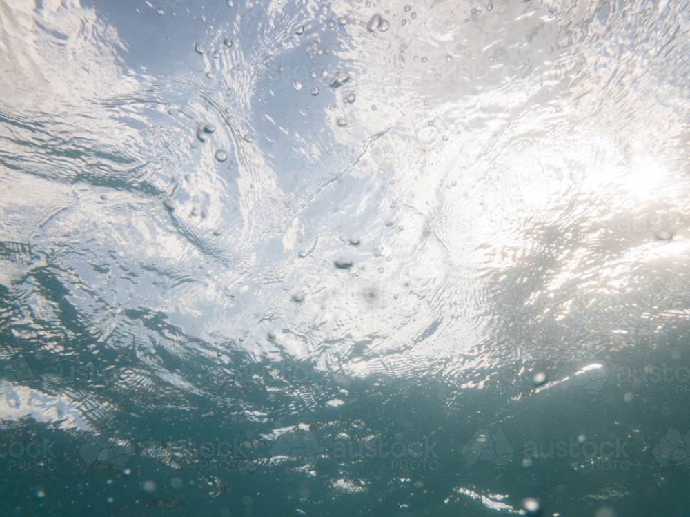 Underwater shot looking up towards the surface through water ripples and bubbles - Australian Stock Image