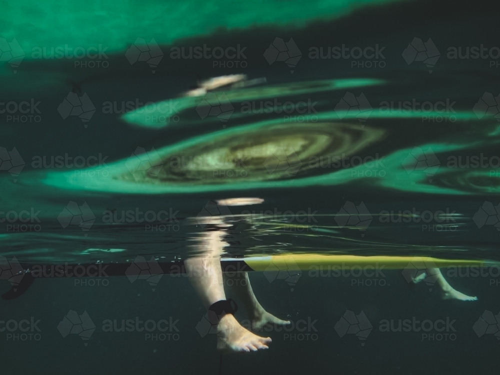 Underwater surfers pair of feet sitting still on surfboard with reflections in water - Australian Stock Image