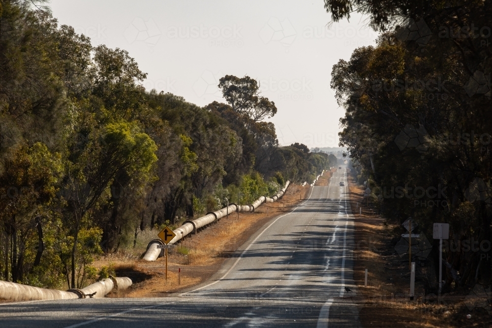 undulating road and water supply pipeline bordered by bush - Australian Stock Image