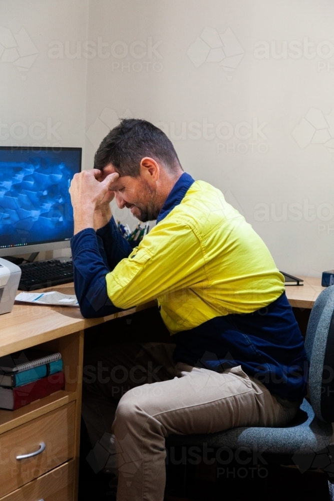 Unhappy tradie stressed out over paperwork in home office - Australian Stock Image