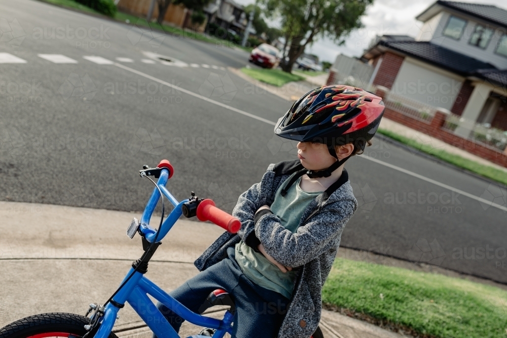 Unhappy young boy with his arms crossed on his bicycle; cycling around his neighbourhood - Australian Stock Image