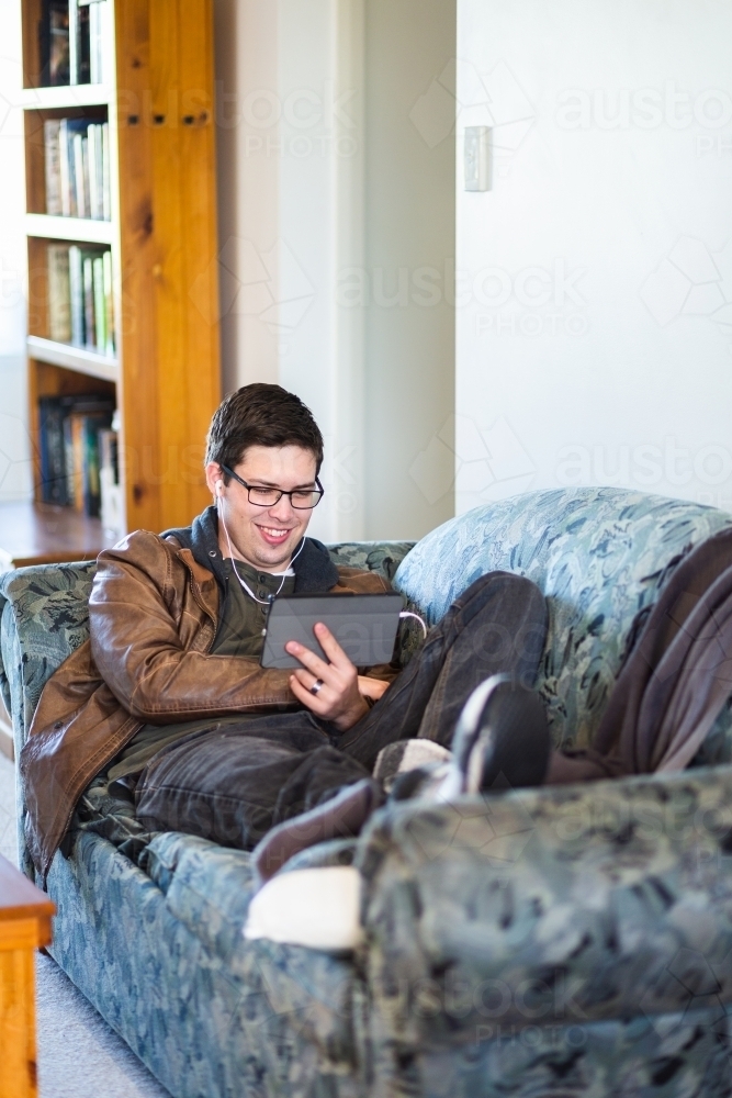 Uni student on tablet relaxing on lounge at home - Australian Stock Image