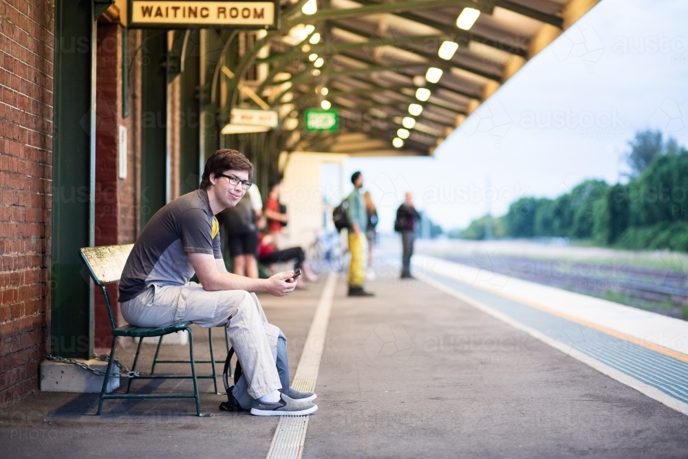 Uni student sitting on bench at train station waiting for train - Australian Stock Image