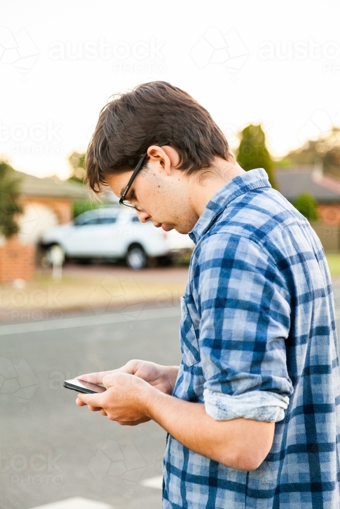 Uni student waiting at bus stop using mobile phone - Australian Stock Image