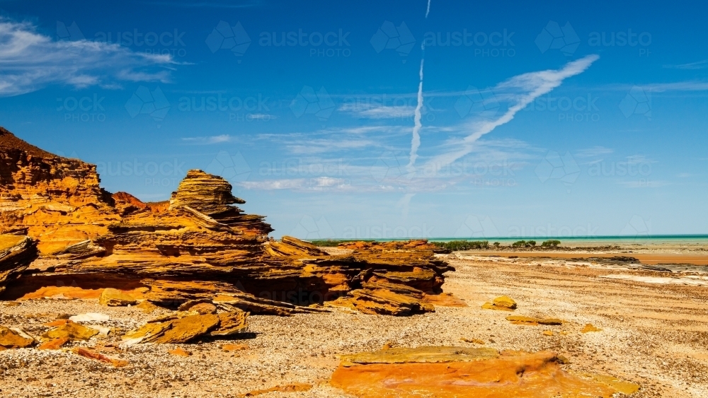 Unusual rocky foreshore at low tide with blue sky and vapour trails - Australian Stock Image