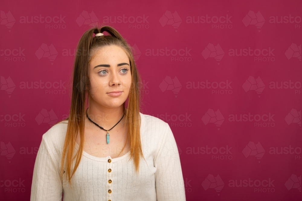 upper body of long-haired teen girl against dark pink background - Australian Stock Image