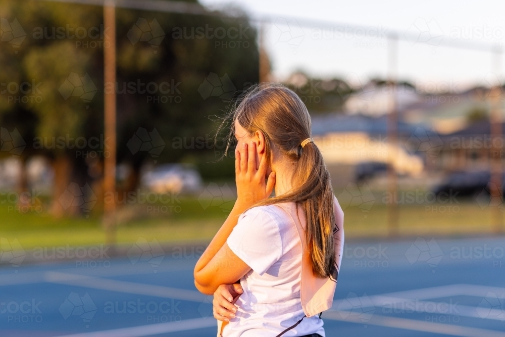upper body of one girl standing with hand to cheek on netball court - Australian Stock Image