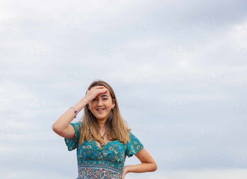 upper body of teenage girl with hand on hip and shading eyes with clouds in background - Australian Stock Image