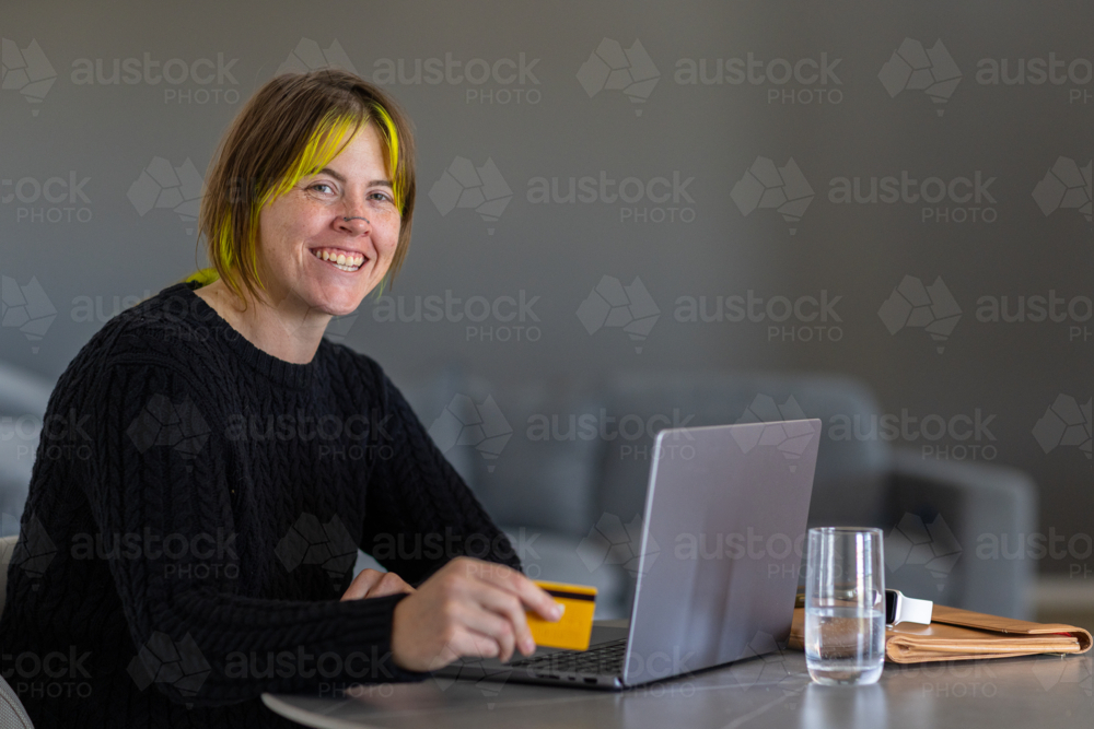 upper body of woman in black sitting at table with laptop computer and credit card - Australian Stock Image
