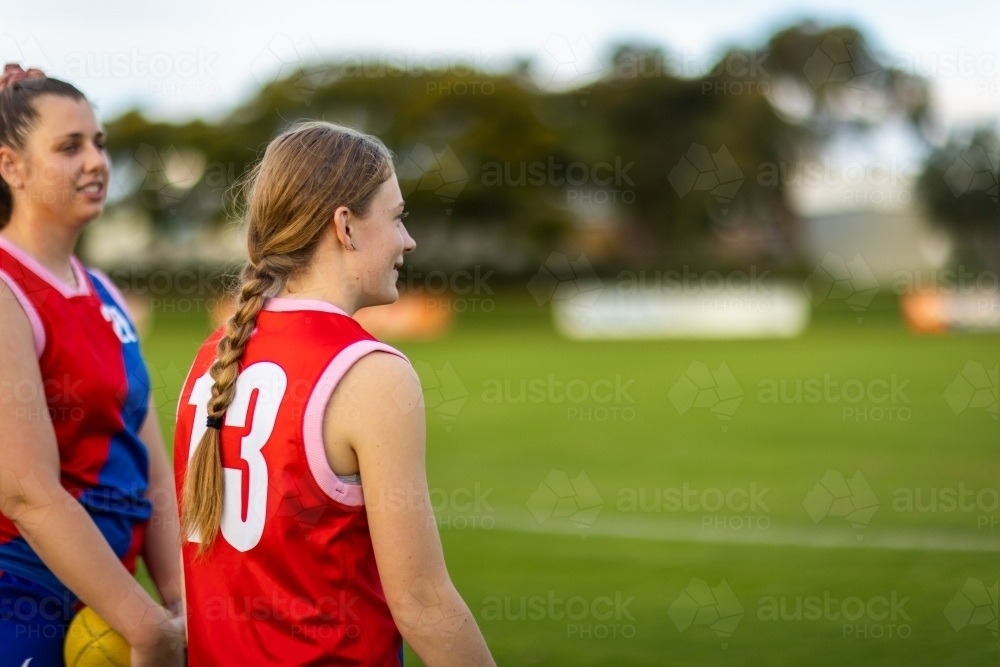 upper body view in profile a couple of female football players on the sidelines of a football oval - Australian Stock Image