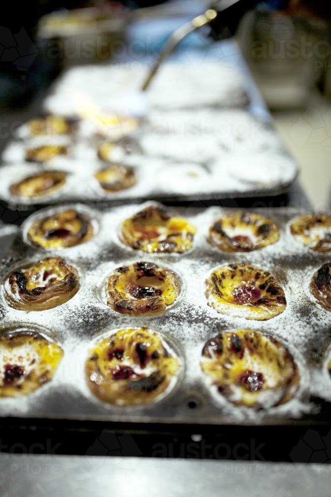 Using blow torch to caramelise freshly made Portugese tarts in tin at bakery cafe - Australian Stock Image
