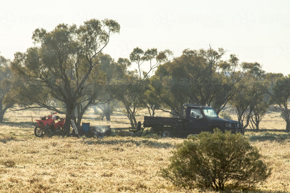 Ute and motorbikes parted near a campfire amongst gidgea trees - Australian Stock Image