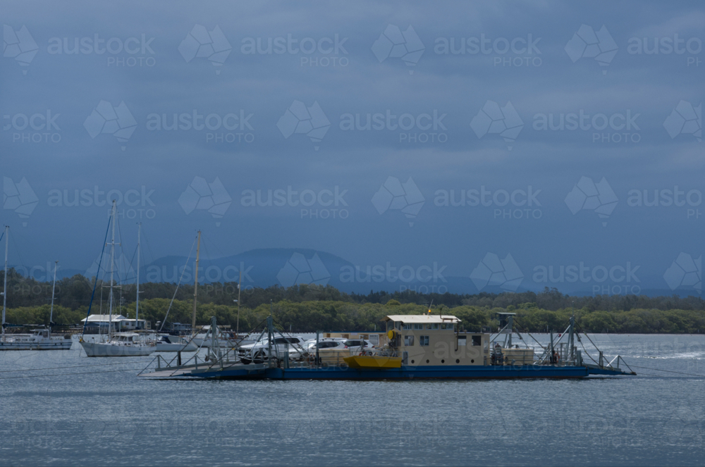 Vehicle ferry crossing river in sun, clouds and boats in background - Australian Stock Image