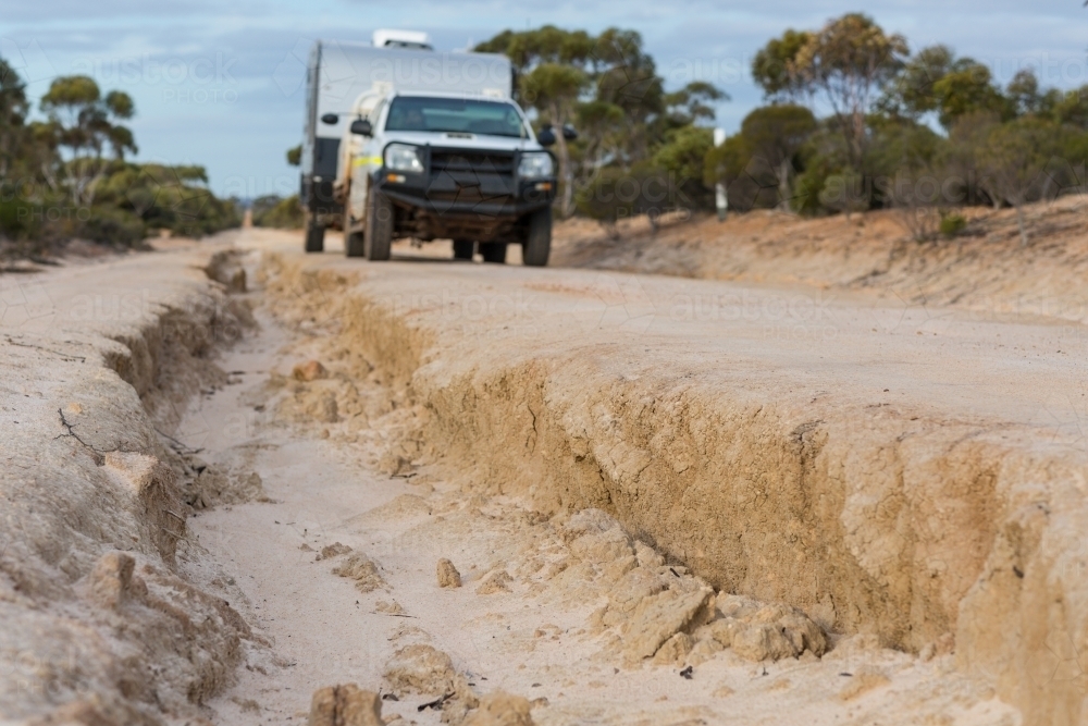 Vehicle towing caravan on washed out dirt track - Australian Stock Image