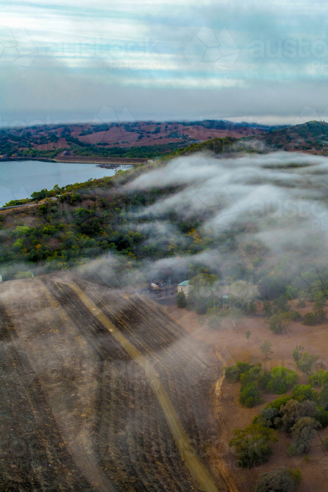 Vertical Aerial image of the Glenbawn Dam wall with morning fog drifting through the valley - Australian Stock Image