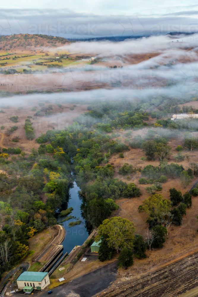 Vertical Aerial image of the Glenbawn Dam wall with morning fog drifting through the valley - Australian Stock Image