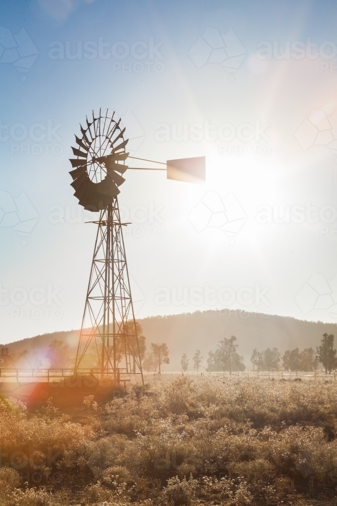 Vertical image of old windmill on farm, backlit with sun star flare - Australian Stock Image