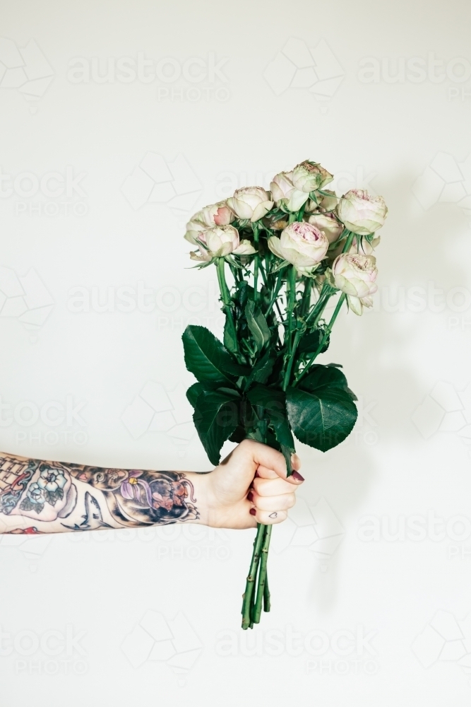 Vertical of a girl's arm with tattoo's holding a bunch of pink roses - Australian Stock Image