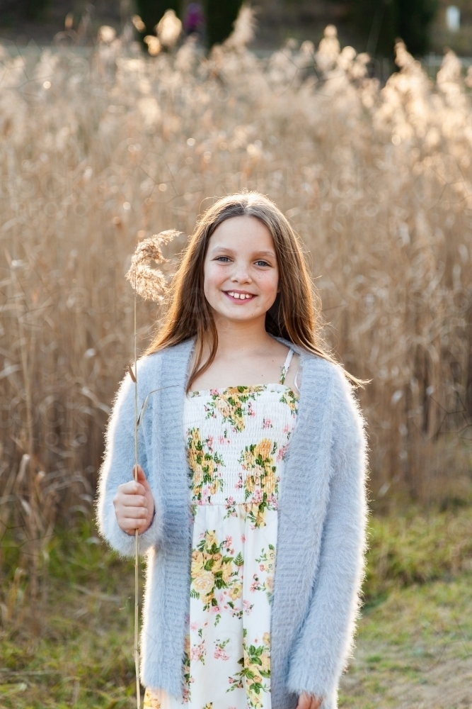 Vertical portrait of a ten year old girl holding bulrush seed outside - Australian Stock Image