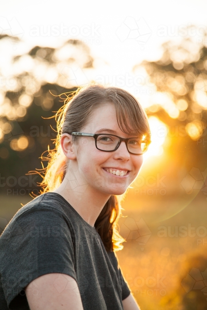 Vertical portrait of a young person with glasses smiling in rural Australia with golden sun flare - Australian Stock Image