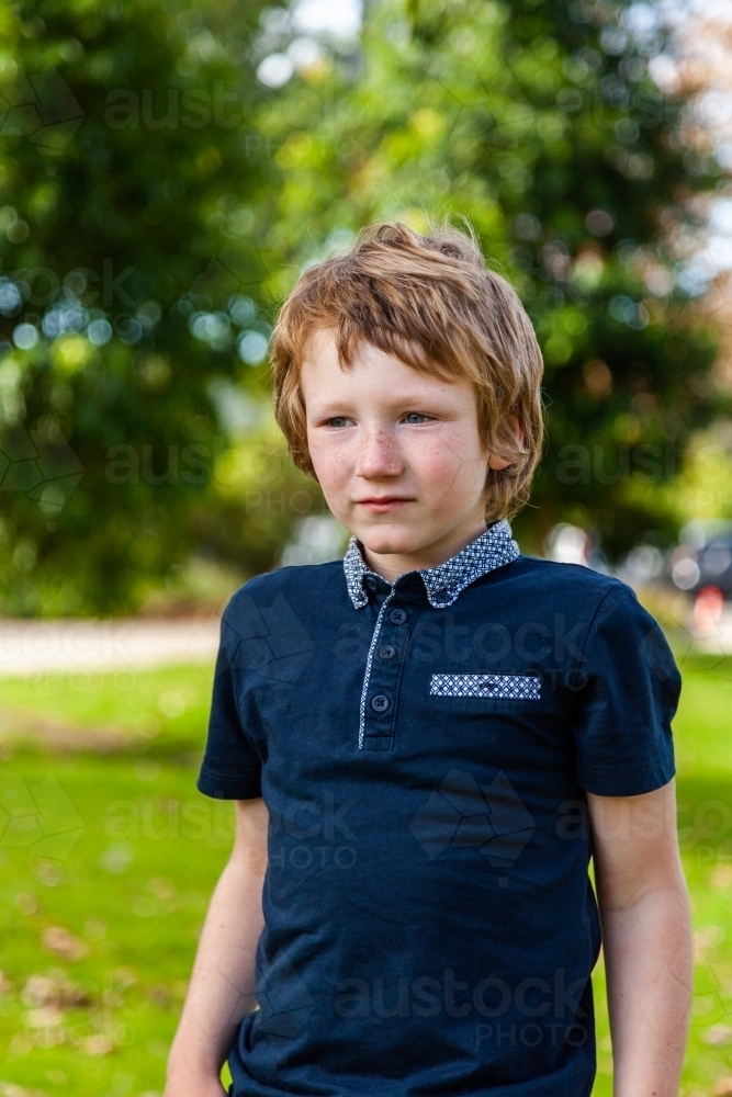 vertical portrait of unsure little autistic boy at park outside - Australian Stock Image