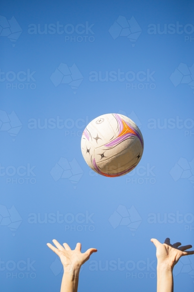 Image of vertical shot of a ball thrown up in the air by two hands with clear skies in the