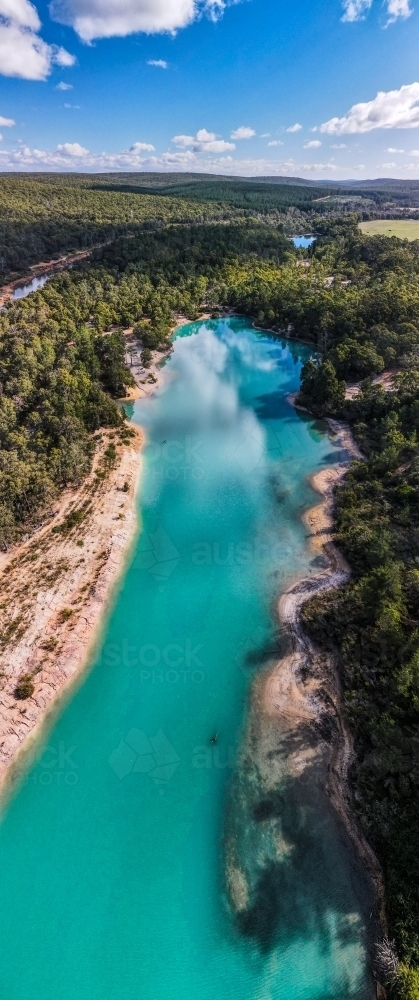 vertical shot of a blue lake surrounded with green trees on a sunny day with white and blue skies - Australian Stock Image