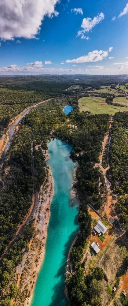 vertical shot of a blue lake surrounded with green trees on a sunny day with white and blue skies - Australian Stock Image
