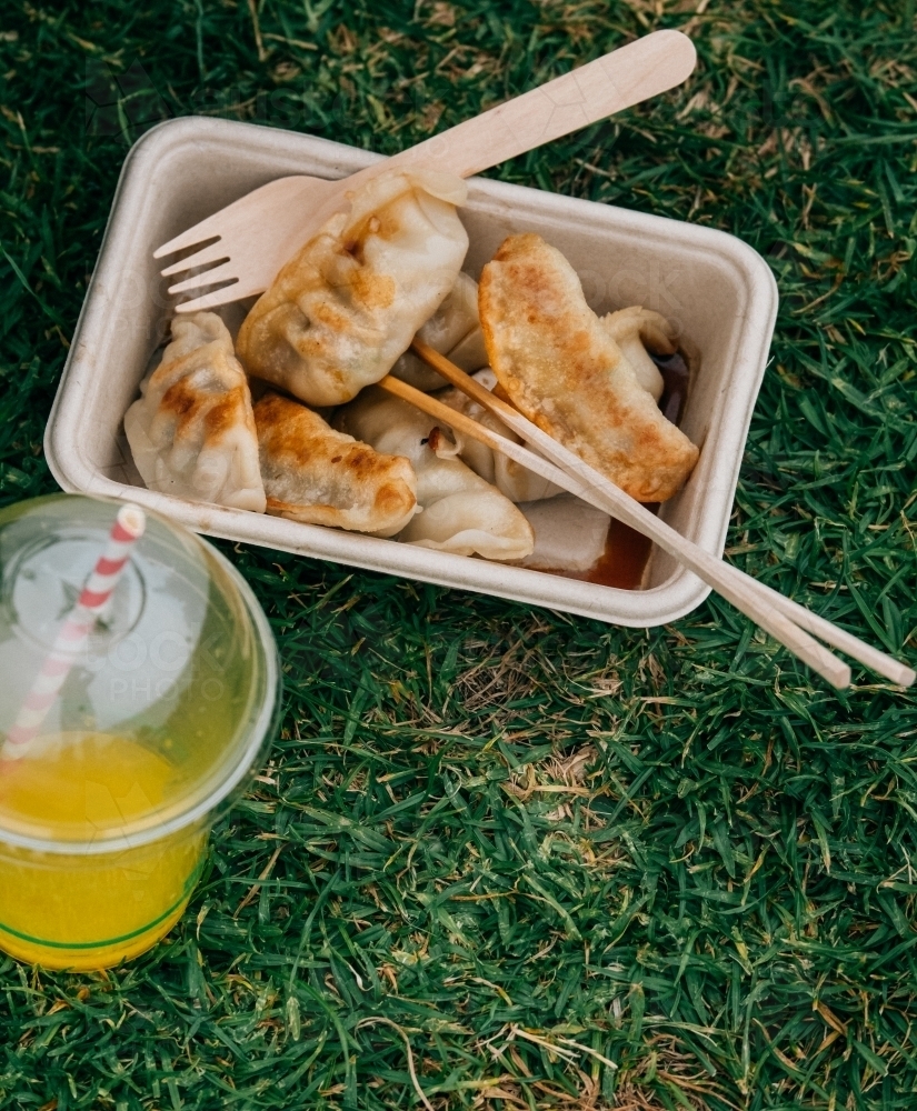 Vertical shot of a food container with dumplings and cutleries with an orange drink on the side - Australian Stock Image