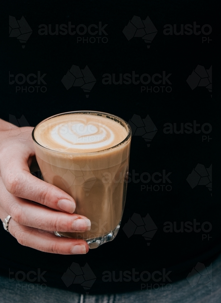 Vertical shot of a hand holding a glass of coffee with coffee art - Australian Stock Image