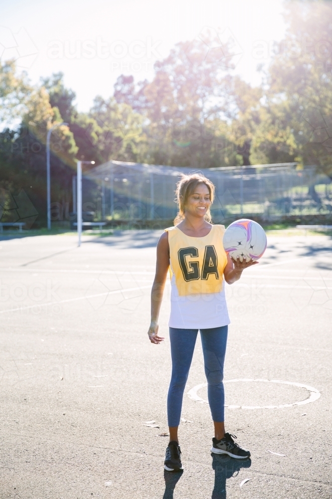 vertical shot of a Indian woman in sportswear holding a net ball on a sunny day - Australian Stock Image