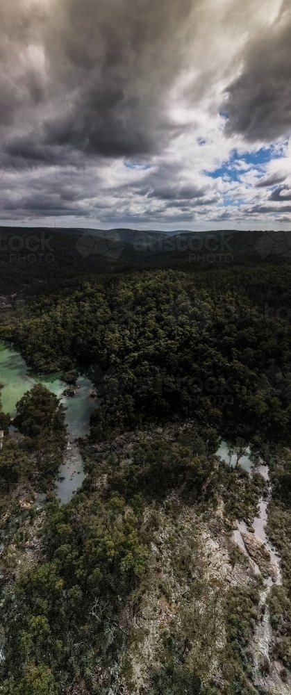 vertical shot of a lake surrounded by bush hills with green trees on a cloudy day with grey skies - Australian Stock Image