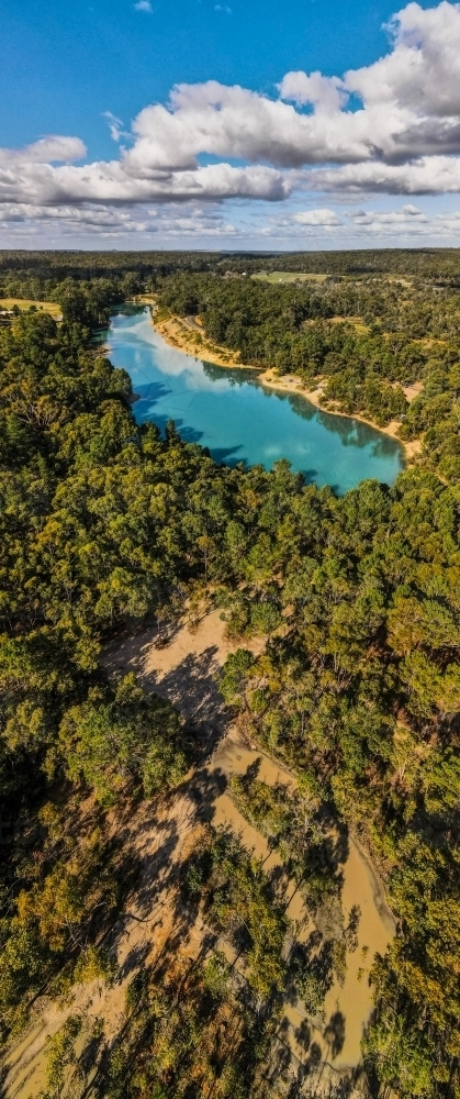vertical shot of a lake surrounded by bush hills with green trees on a sunny day with blue skies - Australian Stock Image