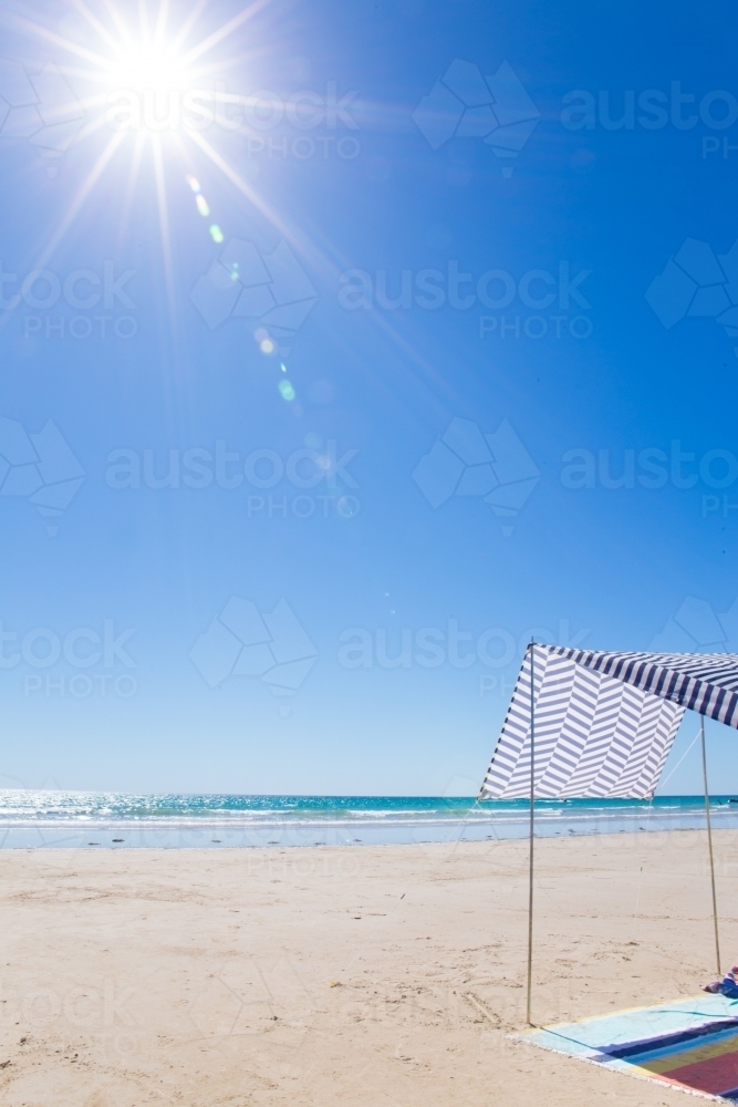 Vertical shot of a sun shelter and beach towel on empty beach on a summer's day - Australian Stock Image