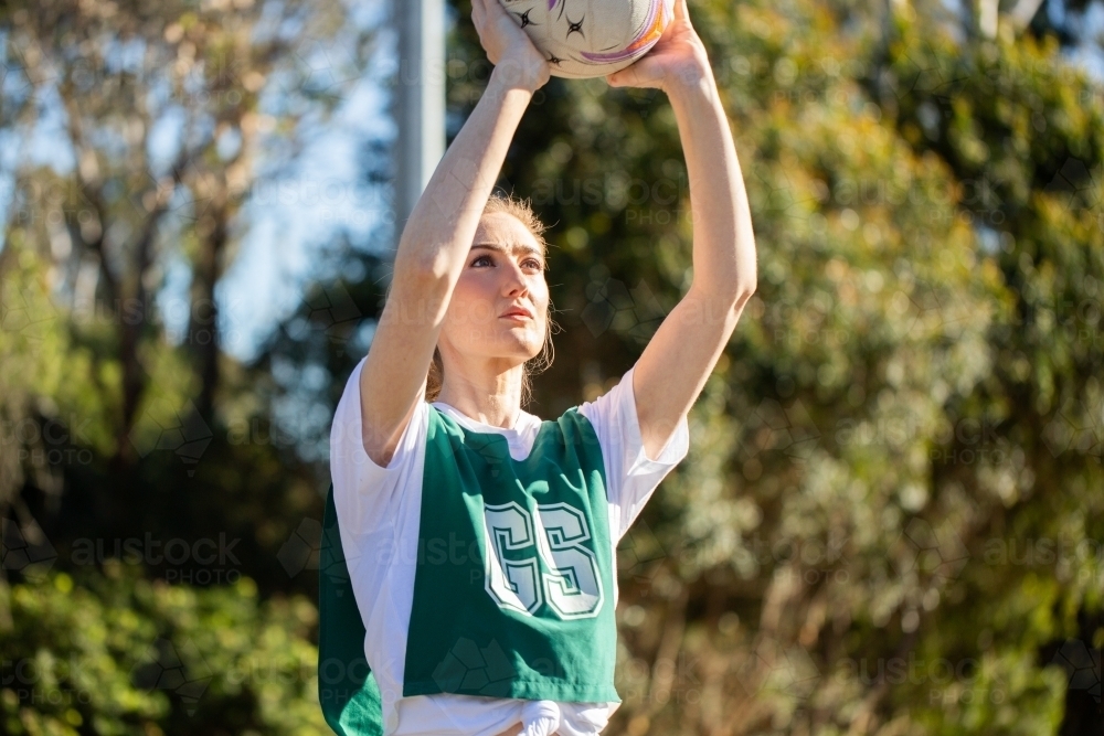 vertical shot of a young woman wearing sports clothes holding a ball up in the air on a sunny day - Australian Stock Image