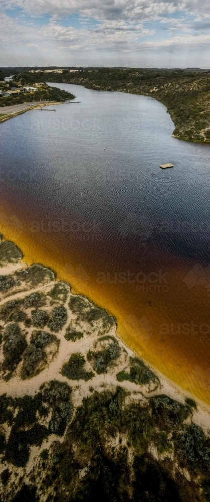vertical shot of an island with boat floating, bushes, yellow sand on a sunny day - Australian Stock Image