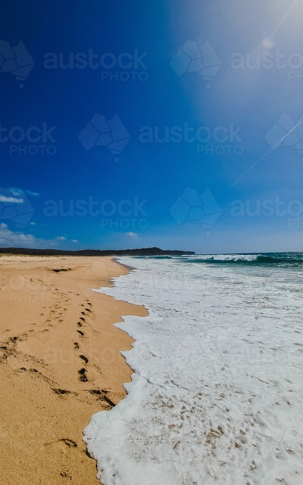 Vertical shot of gentle waves lapping sand at the beach - Australian Stock Image