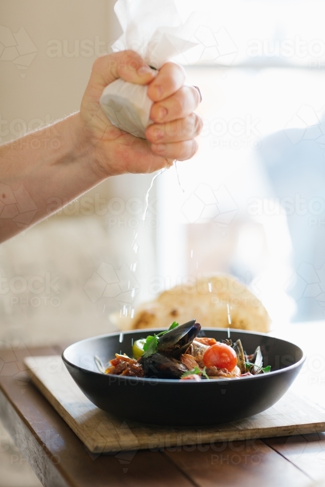 Vertical shot of hand squeezing a lemon wrapped in a white piece of cloth to a bowl of seafood - Australian Stock Image