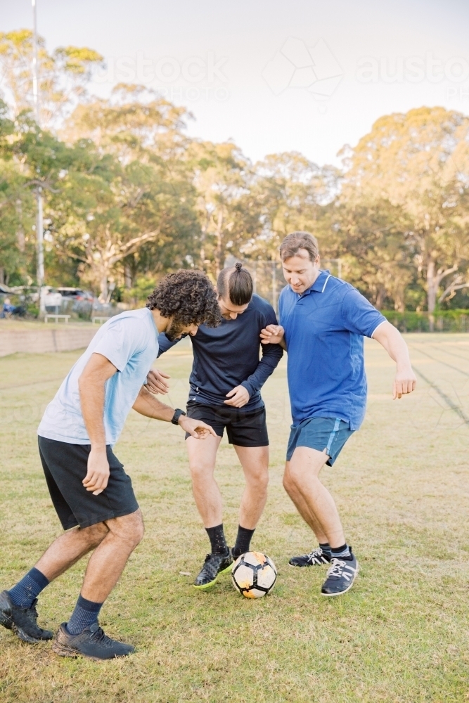vertical shot of men playing soccer in the field on a sunny day with clear skies - Australian Stock Image
